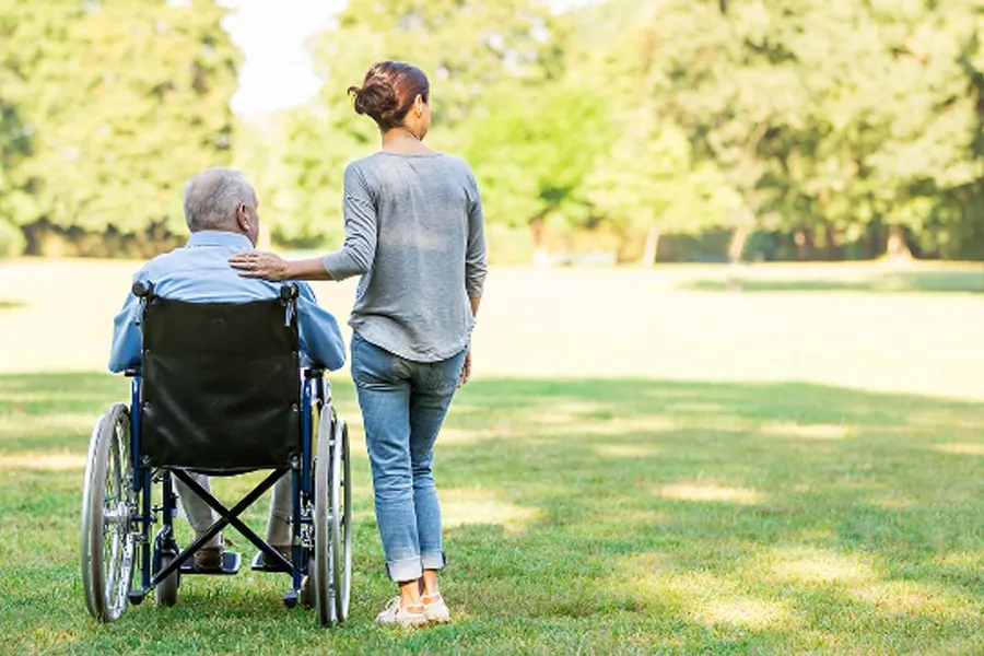 Une intervenante marche au parc avec un résident en fauteuil roulant